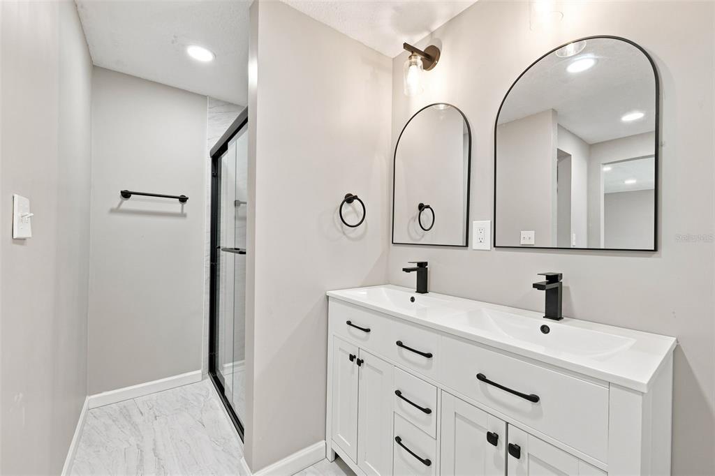 A bathroom features a double vanity with white cabinets, black fixtures, and two arched mirrors — 4025 STRATFIELD DRIVE, NEW PORT RICHEY, FL