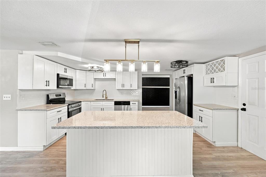 A bright kitchen features white cabinets, a large granite-topped island, and stainless steel appliances — 4025 STRATFIELD DRIVE, NEW PORT RICHEY, FL