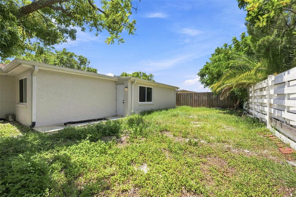 The exterior of a beige house features a small concrete patio and an overgrown yard — 4025 STRATFIELD DRIVE, NEW PORT RICHEY, FL