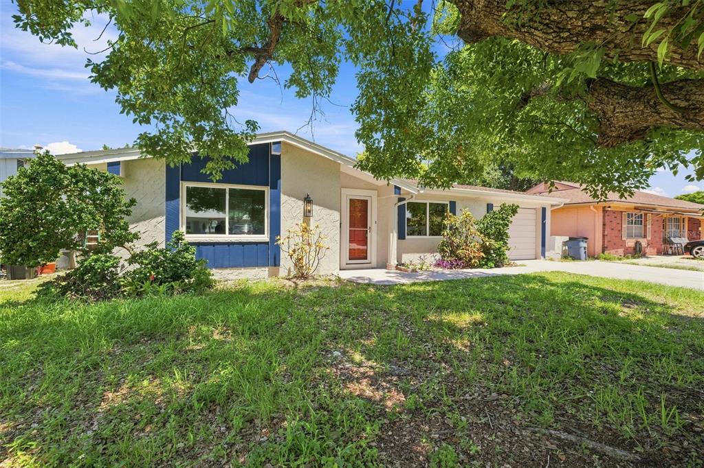 A single-story house with a blue accent wall, white siding, and a large tree in front — 4025 STRATFIELD DRIVE, NEW PORT RICHEY, FL