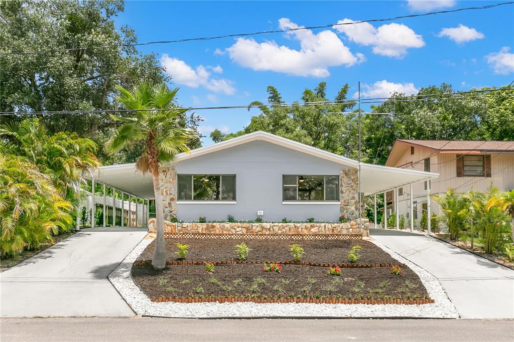 A single-story duplex with gray siding, stone accents, and two side-by-side carports — 1435 WEGMANN DRIVE, TARPON SPRINGS, FL