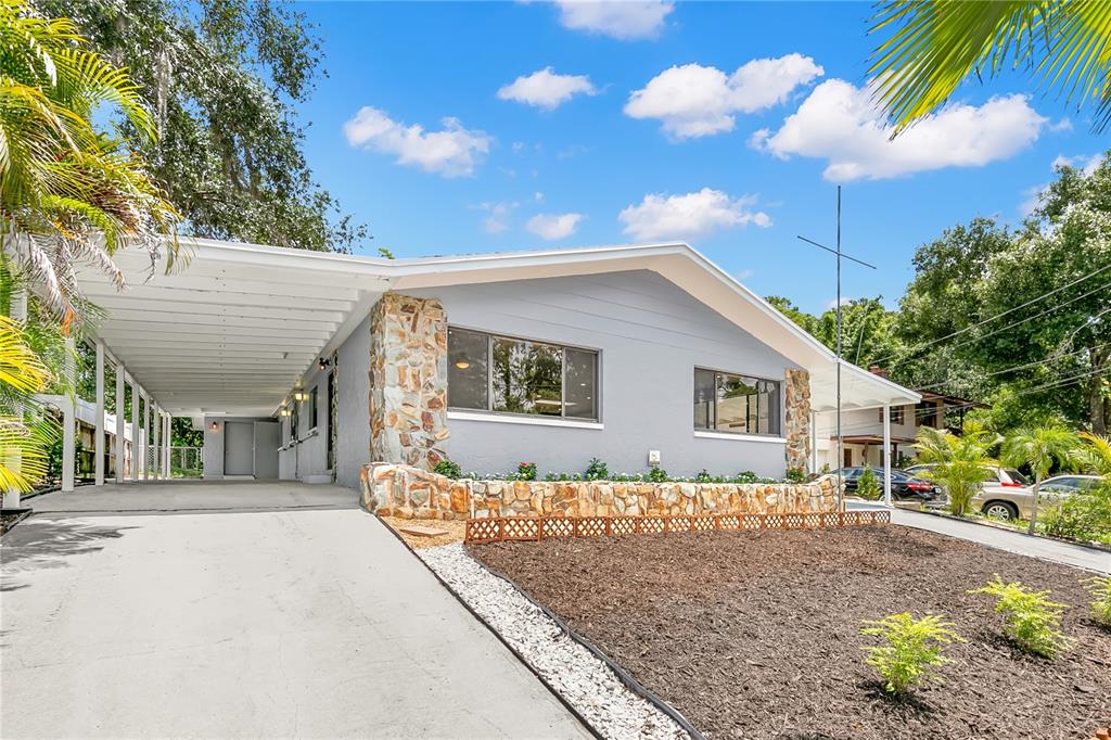 A single-story house with a gray exterior, stone accents, and a large attached carport — 1435 WEGMANN DRIVE, TARPON SPRINGS, FL