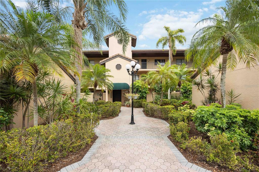 A paved walkway leads to the entrance of a multi-story building surrounded by palm trees — 5627 ASHTON WAY UNIT 5627, SARASOTA, FL
