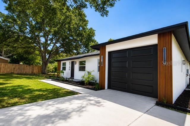 A white house with a black garage door and wood-slat accents sits on a grassy lot — 5140 TREND ROAD, WEST MELBOURNE, FL
