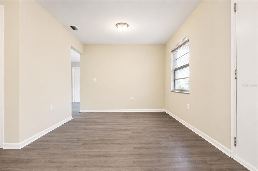 An empty room with light-colored walls, wood-look flooring, a single window, and a ceiling light — 4348 BLACK FOX DRIVE, NEW PORT RICHEY, FL