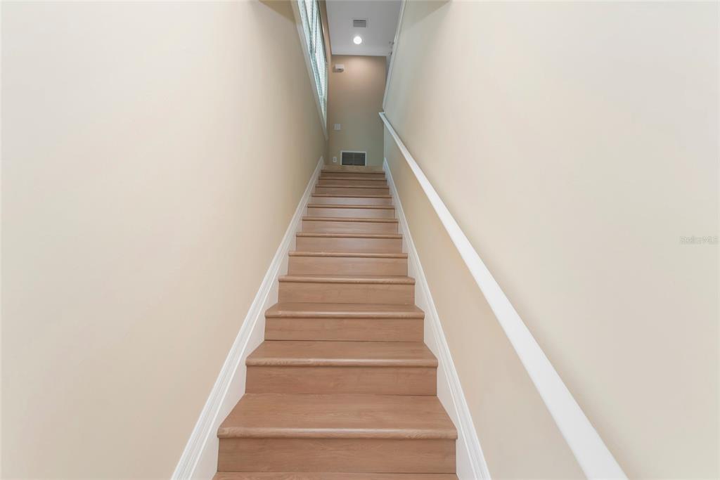 A straight wooden staircase with white railings leads upward between two beige walls — 4296 EXPEDITION WAY UNIT 104, OSPREY, FL