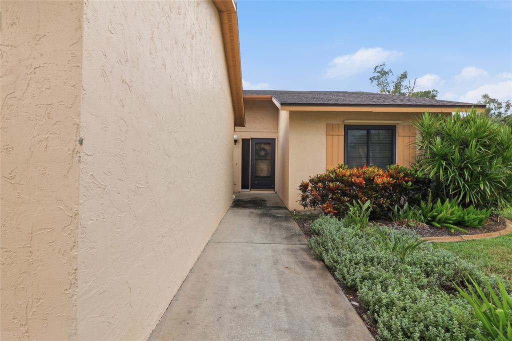 A concrete walkway leads to the front entrance of a single-story house with tan stucco — 3191 GLEN ELYN BOULEVARD UNIT 4, SARASOTA, FL