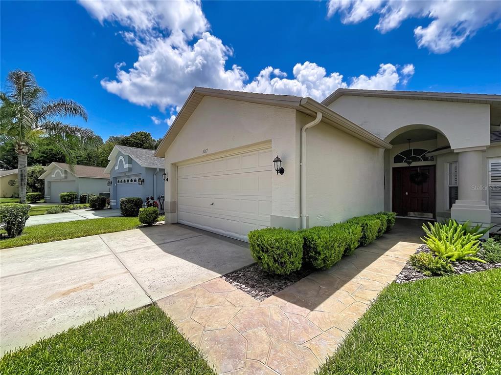 A beige single-story house features a two-car garage, a stone walkway, and manicured landscaping — 1017 SWEET JASMINE DRIVE, TRINITY, FL
