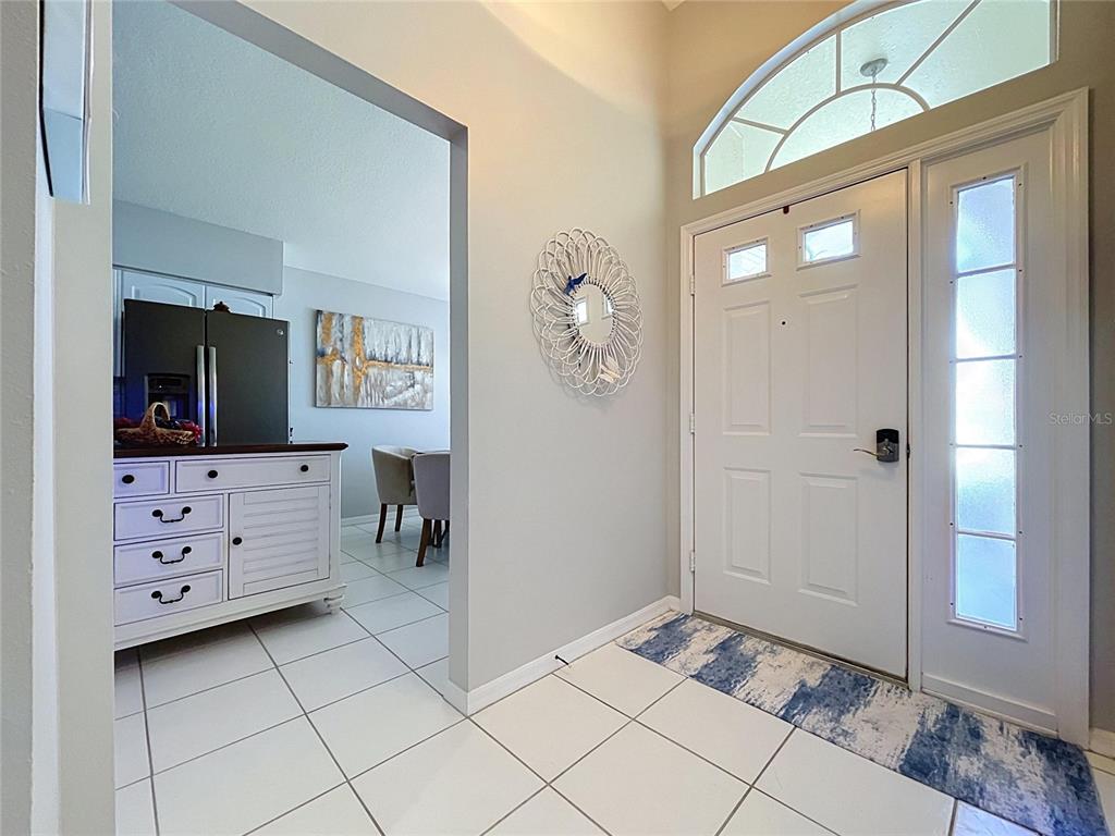 A white front door with a sidelight and transom window opens into a tiled entryway — 1017 SWEET JASMINE DRIVE, TRINITY, FL