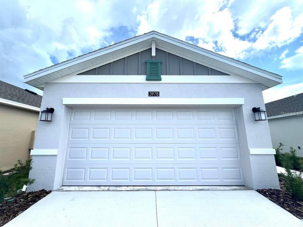 A light-colored house exterior features a white garage door, a gable roof, and two sconces — 3978 AMBROSE AVENUE, KISSIMMEE, FL