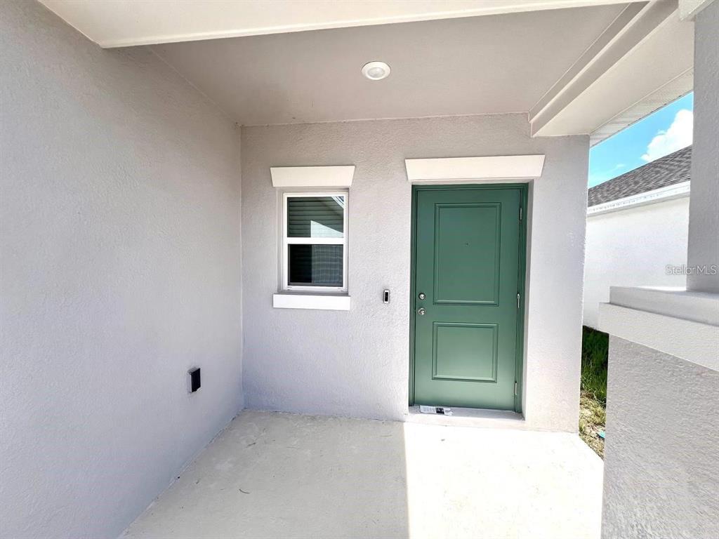 A covered concrete porch features a green front door and a single window — 3978 AMBROSE AVENUE, KISSIMMEE, FL