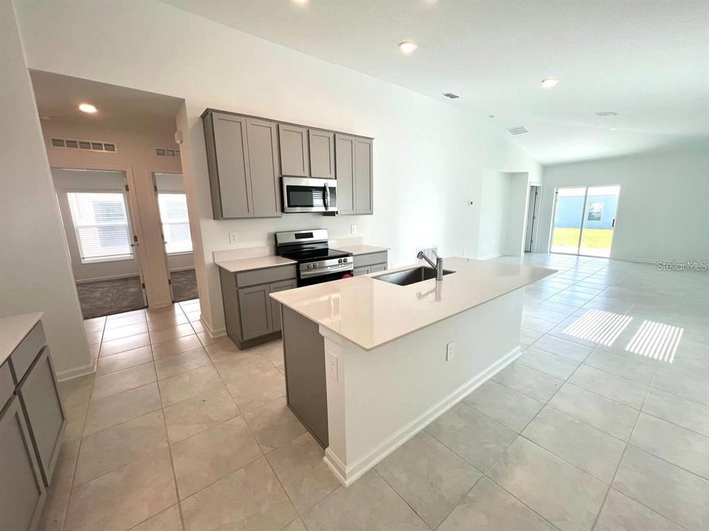 A modern kitchen features gray cabinets, white countertops, a central island, and light tile flooring — 3978 AMBROSE AVENUE, KISSIMMEE, FL