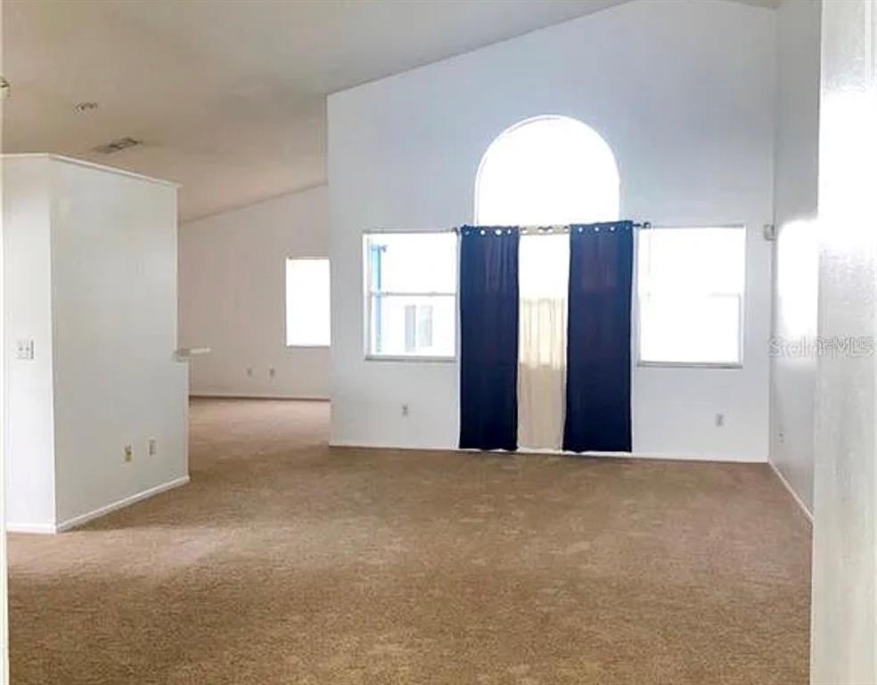 A spacious living room features beige carpeting, white walls, and a large arched window — 12533 DARBY AVENUE, ORLANDO, FL