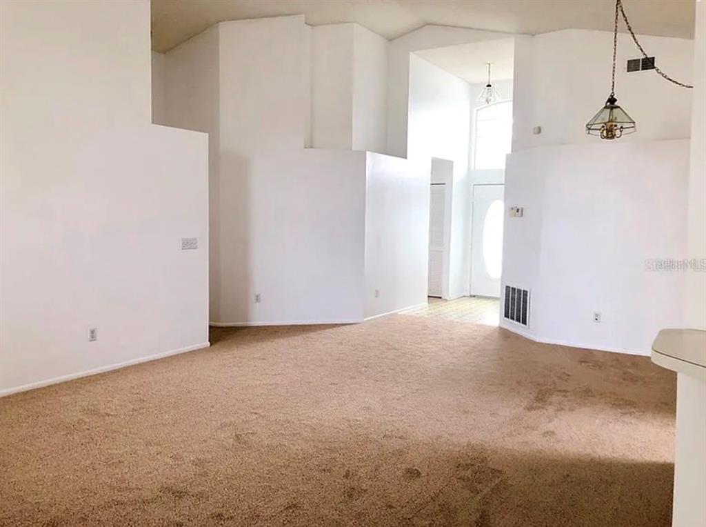 An empty living room features high ceilings, beige carpeting, and a view of the entryway — 12533 DARBY AVENUE, ORLANDO, FL