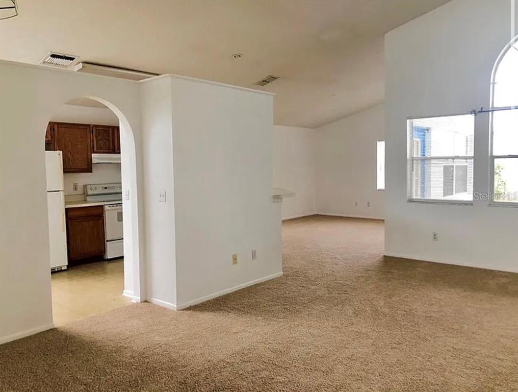 An interior view shows a carpeted living area with vaulted ceilings and an arched kitchen entrance — 12533 DARBY AVENUE, ORLANDO, FL