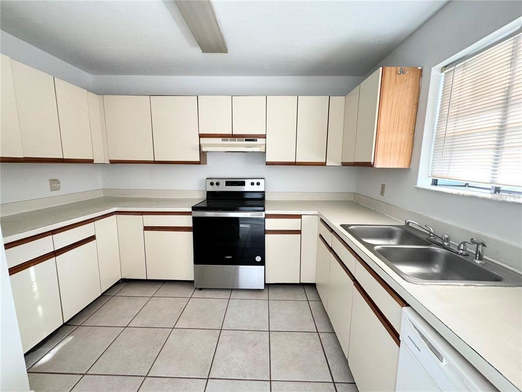 A kitchen features white cabinets, laminate countertops, a stainless steel stove, and tiled flooring — 2300 SW 43RD STREET UNIT M4, GAINESVILLE, FL