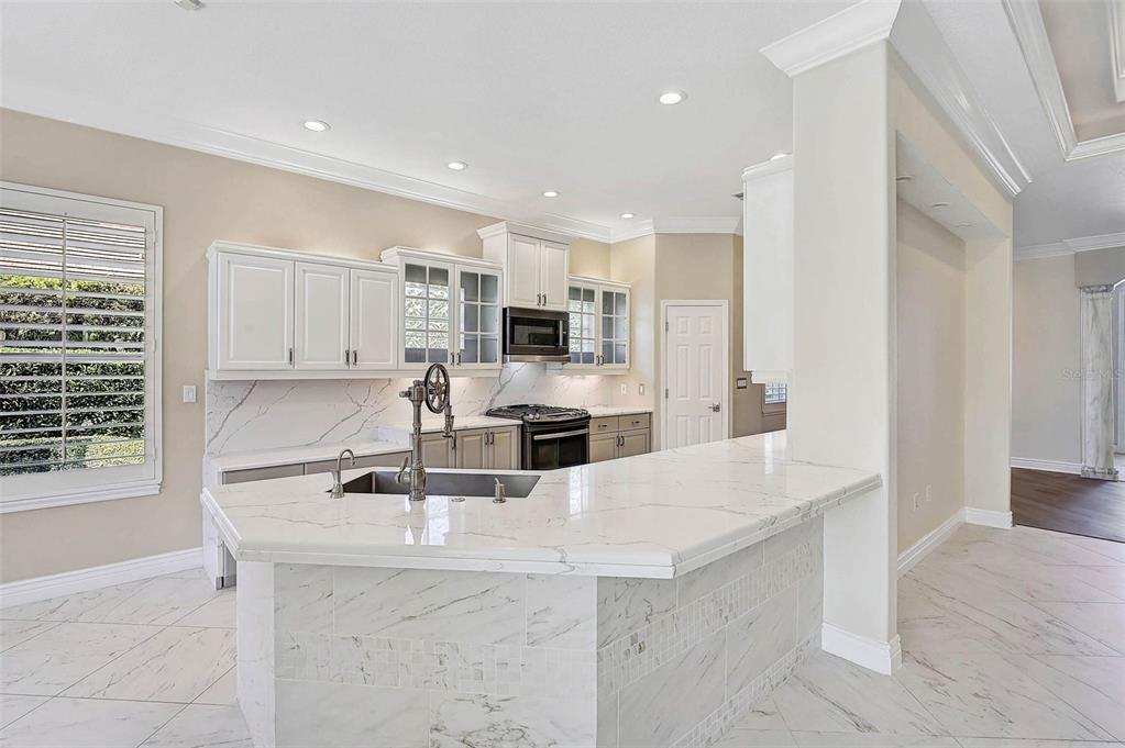 A kitchen features white cabinets, marble-look countertops, a central island, and light-colored tile flooring — 13 BAYHEAD LANE, OSPREY, FL