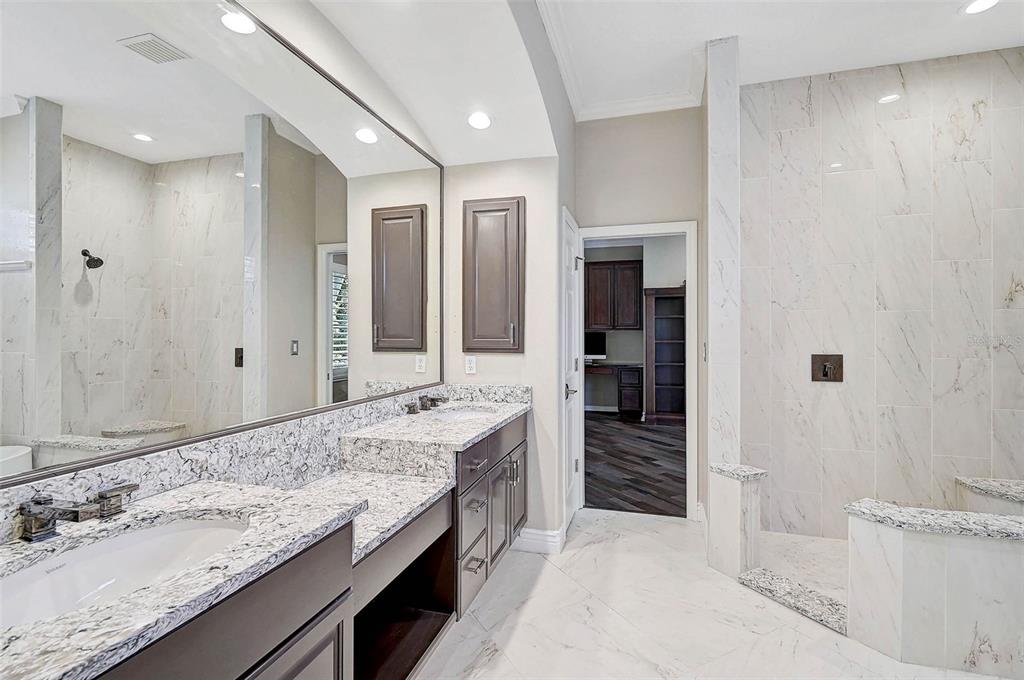 A bathroom with a double vanity, granite countertops, dark cabinets, and a walk-in tiled shower — 13 BAYHEAD LANE, OSPREY, FL