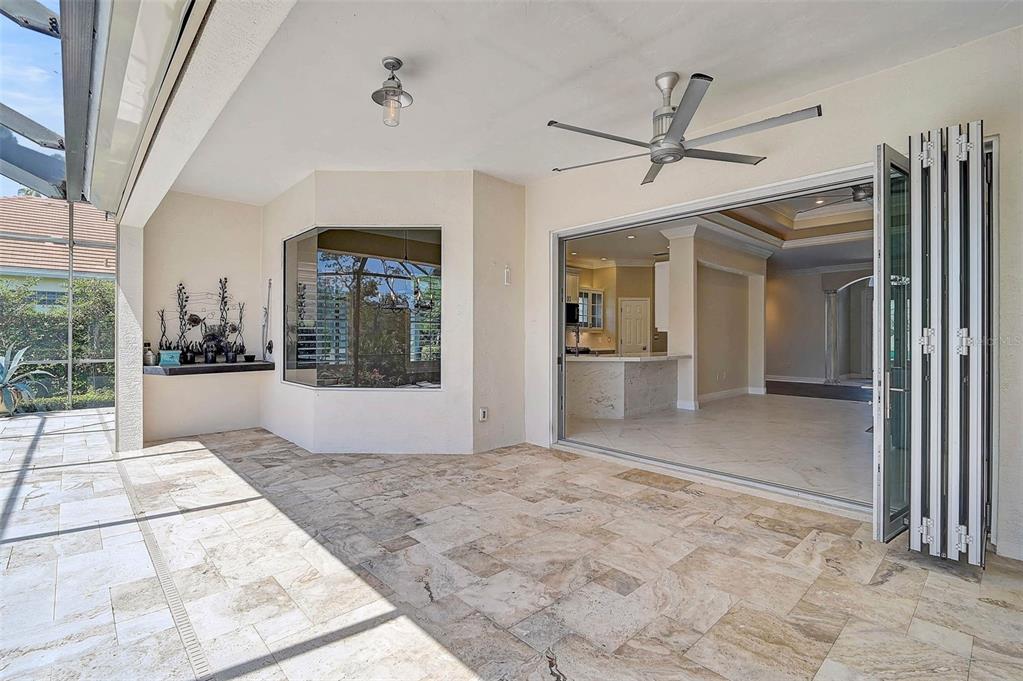 A covered patio with stone flooring features a ceiling fan and folding glass doors — 13 BAYHEAD LANE, OSPREY, FL