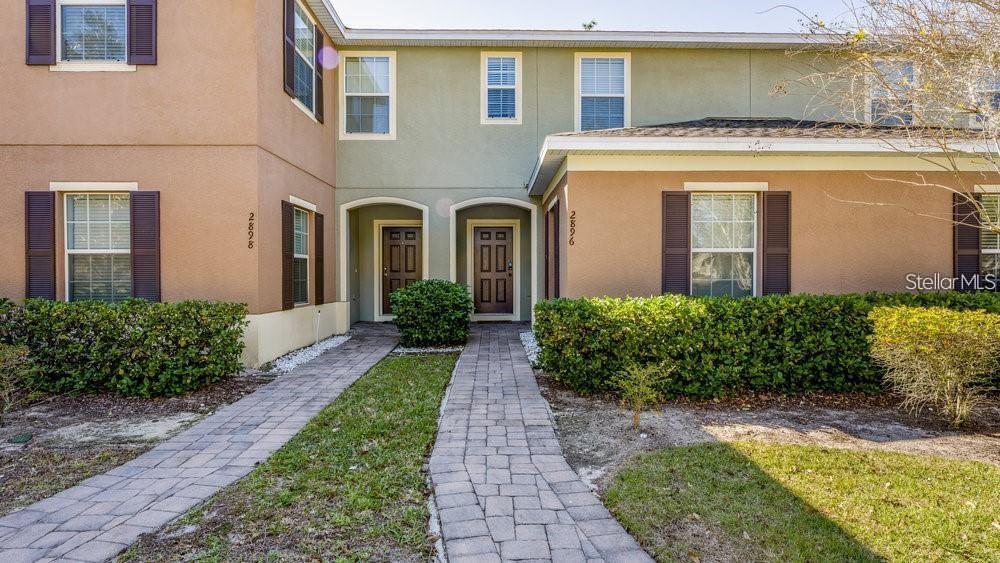 A two-story townhouse exterior features tan and green siding with brick walkways and landscaping — 2896 TANZANITE TERRACE, KISSIMMEE, FL