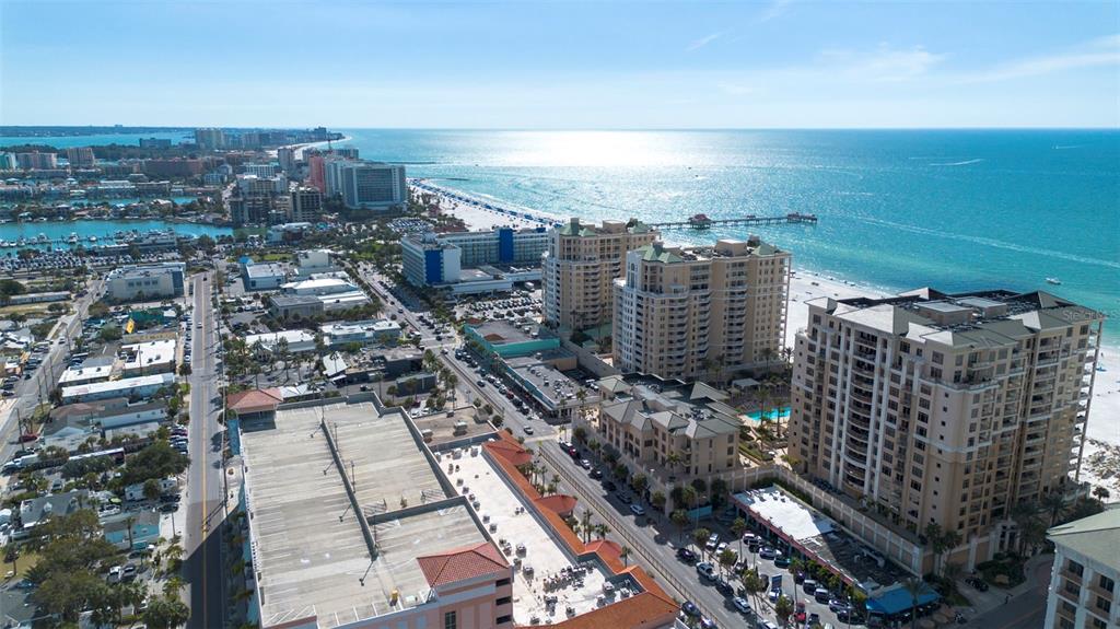 An aerial view shows a coastal city with high-rise buildings, a beach, and a pier — 470 MANDALAY AVENUE UNIT 303, CLEARWATER, FL