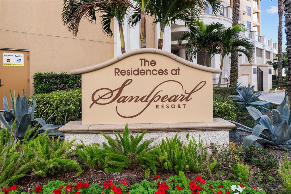 A beige monument sign for The Residences at Sandpearl Resort stands in a landscaped garden — 470 MANDALAY AVENUE UNIT 303, CLEARWATER, FL