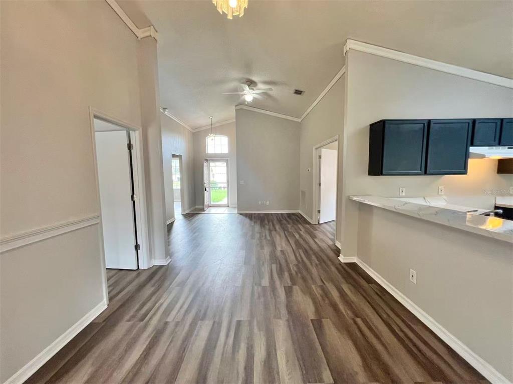An interior view shows a living area with wood-look flooring, vaulted ceilings, and a kitchen — 1275 ADIRONDACK COURT, APOPKA, FL