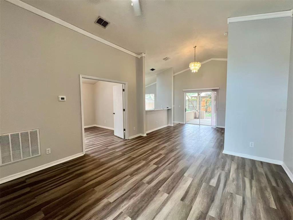 A living room with wood-look flooring, vaulted ceilings, a chandelier, and a sliding glass door — 1275 ADIRONDACK COURT, APOPKA, FL