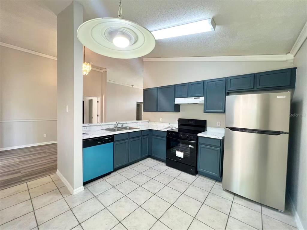 A kitchen features dark blue cabinets, stainless steel appliances, and light-colored tile flooring — 1275 ADIRONDACK COURT, APOPKA, FL