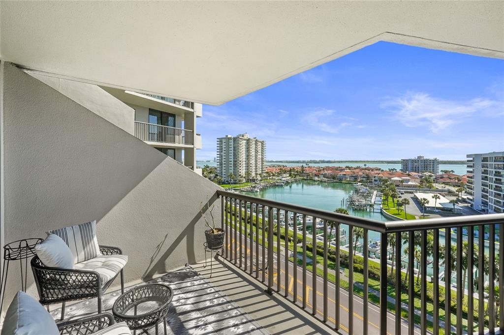 A balcony with outdoor furniture overlooks a marina, a road, and high-rise buildings — 1660 GULF BOULEVARD UNIT 807, CLEARWATER, FL