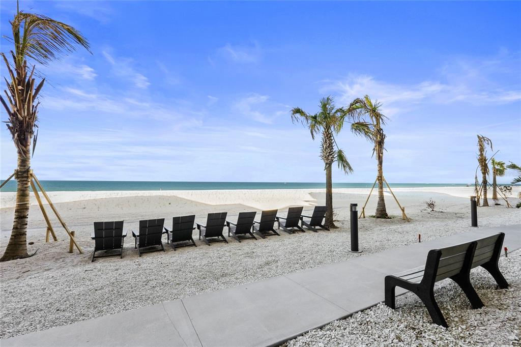 A row of beach chairs sits on a gravel area overlooking the ocean and palms — 1660 GULF BOULEVARD UNIT 807, CLEARWATER, FL