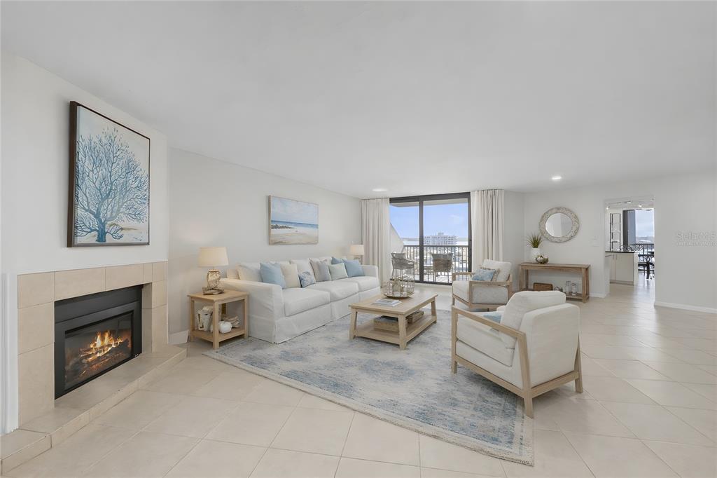 A bright living room features a fireplace, white sofa, armchairs, and a balcony with water views — 1660 GULF BOULEVARD UNIT 807, CLEARWATER, FL