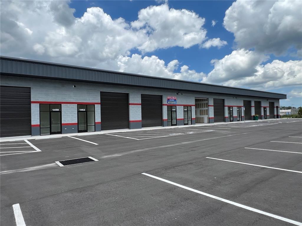 A modern commercial warehouse building with multiple roll-up doors and glass storefronts under a cloudy sky — 1450 HAMLIN AVENUE, ST CLOUD, FL