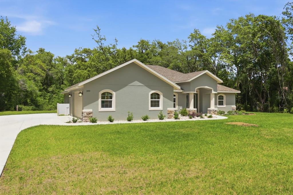 A single-story house with a light green exterior, stone accents, and a concrete driveway — 399 W MASSACHUSETTS STREET, HERNANDO, FL