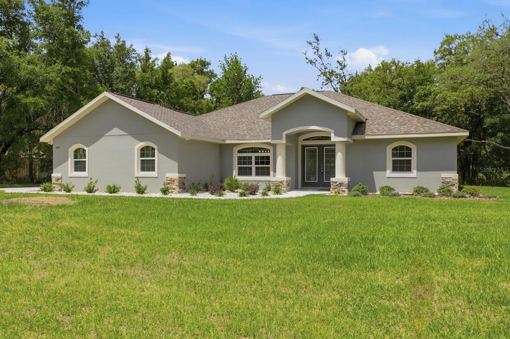 A single-story gray house with stone accents, a covered entryway, and a large front lawn — 399 W MASSACHUSETTS STREET, HERNANDO, FL