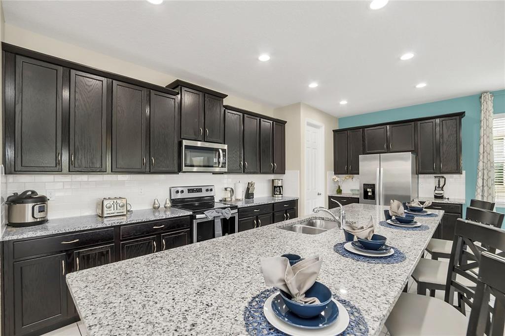 A kitchen features dark wood cabinets, granite countertops, stainless steel appliances, and a large island — 1576 NASSAU POINT TRAIL, KISSIMMEE, FL