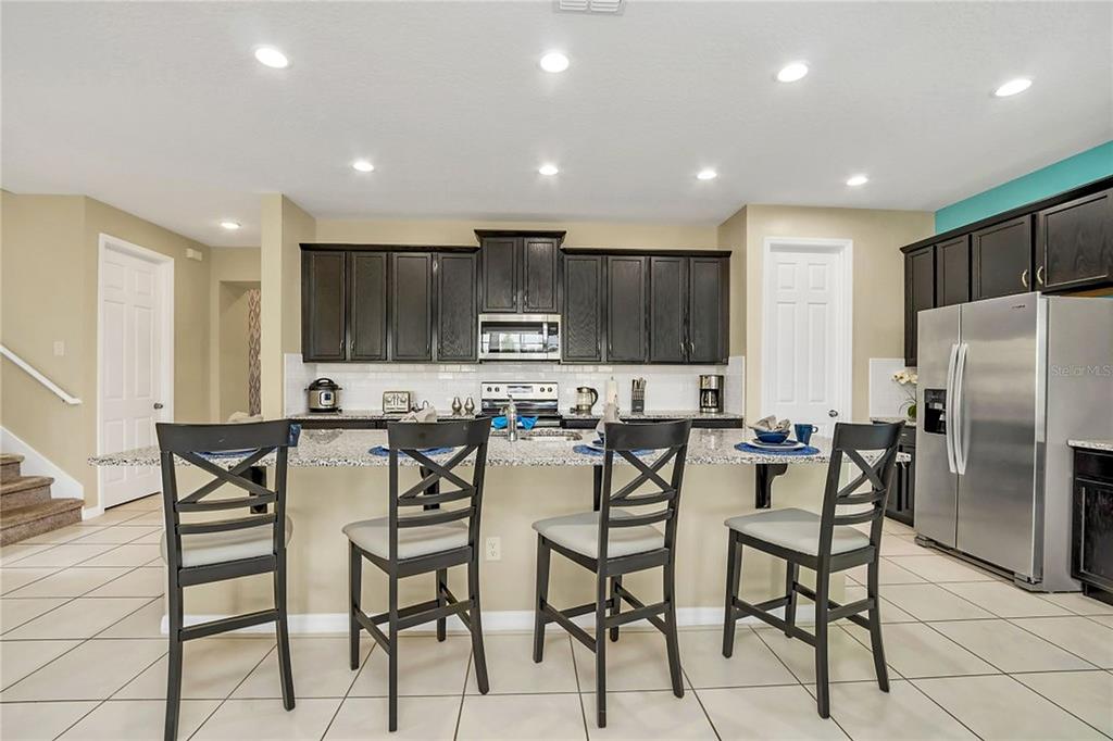 A kitchen features dark wood cabinets, granite countertops, a breakfast bar with four chairs, and stainless-steel appliances — 1576 NASSAU POINT TRAIL, KISSIMMEE, FL