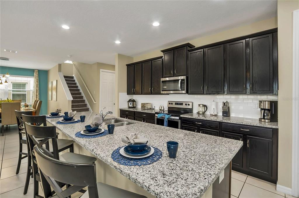 A kitchen with dark cabinets, granite countertops, a large island, and stairs in the background — 1576 NASSAU POINT TRAIL, KISSIMMEE, FL