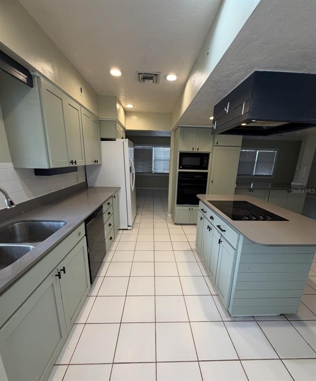 A kitchen features light green cabinets, a central island with a cooktop, and white tile flooring — 3408 17TH AVENUE W, BRADENTON, FL