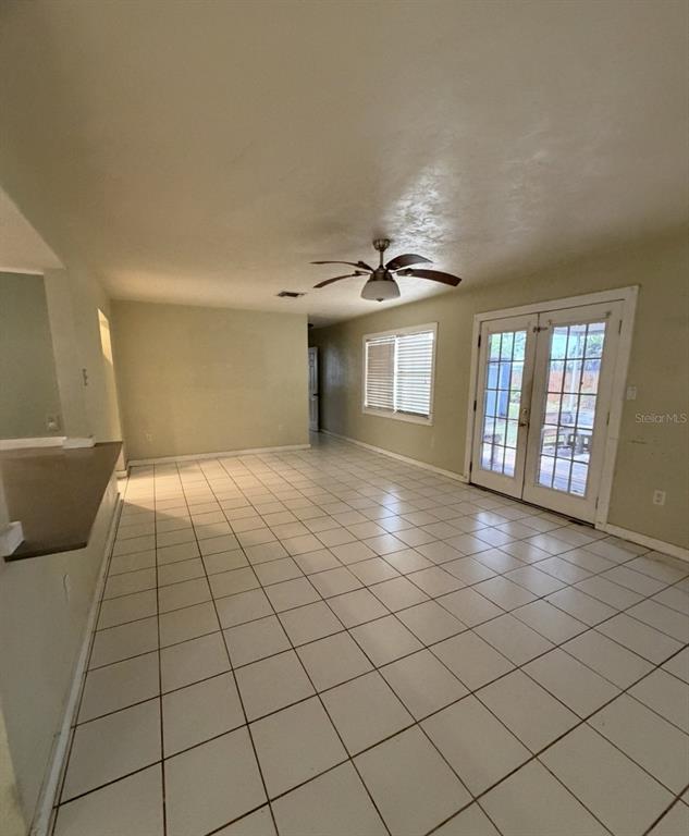 A spacious room with white tile flooring, a ceiling fan, and French doors leading outside — 3408 17TH AVENUE W, BRADENTON, FL