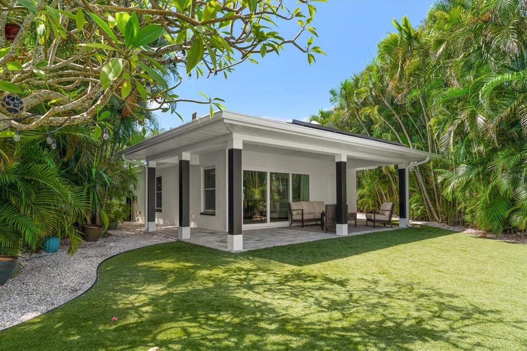 A covered patio with dark pillars overlooks a green lawn surrounded by lush tropical trees — 1907 BAY BOULEVARD, INDIAN ROCKS BEACH, FL