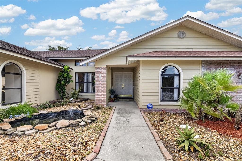 A beige house exterior features a stone-lined pond, a concrete walkway, and arched windows — 2814 HAMMOCK DRIVE, PLANT CITY, FL