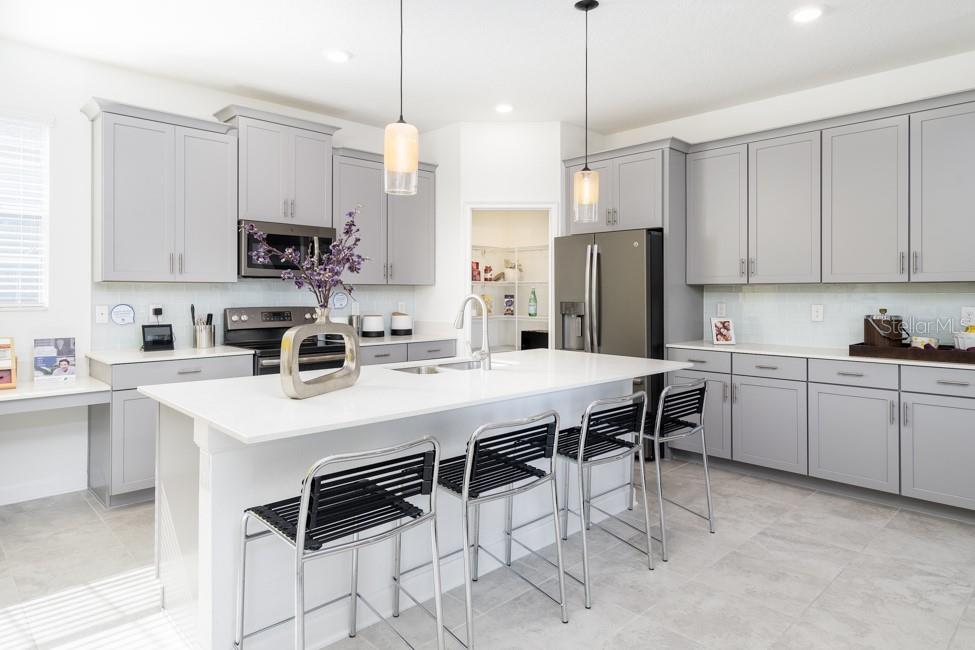 A modern kitchen features gray cabinets, a white island with bar stools, and stainless appliances — 6028 MEDITATION DRIVE, CLERMONT, FL