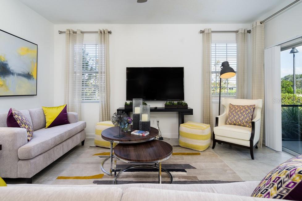A living room features a grey sofa, a white armchair, a television, and nested coffee tables — 6028 MEDITATION DRIVE, CLERMONT, FL