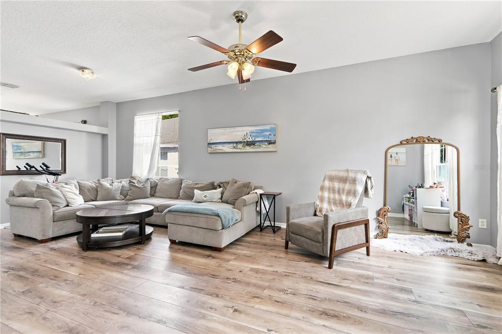 A living room features a sectional sofa, an armchair, a ceiling fan, and wood-look flooring — 1732 NESTLEWOOD TRAIL, ORLANDO, FL