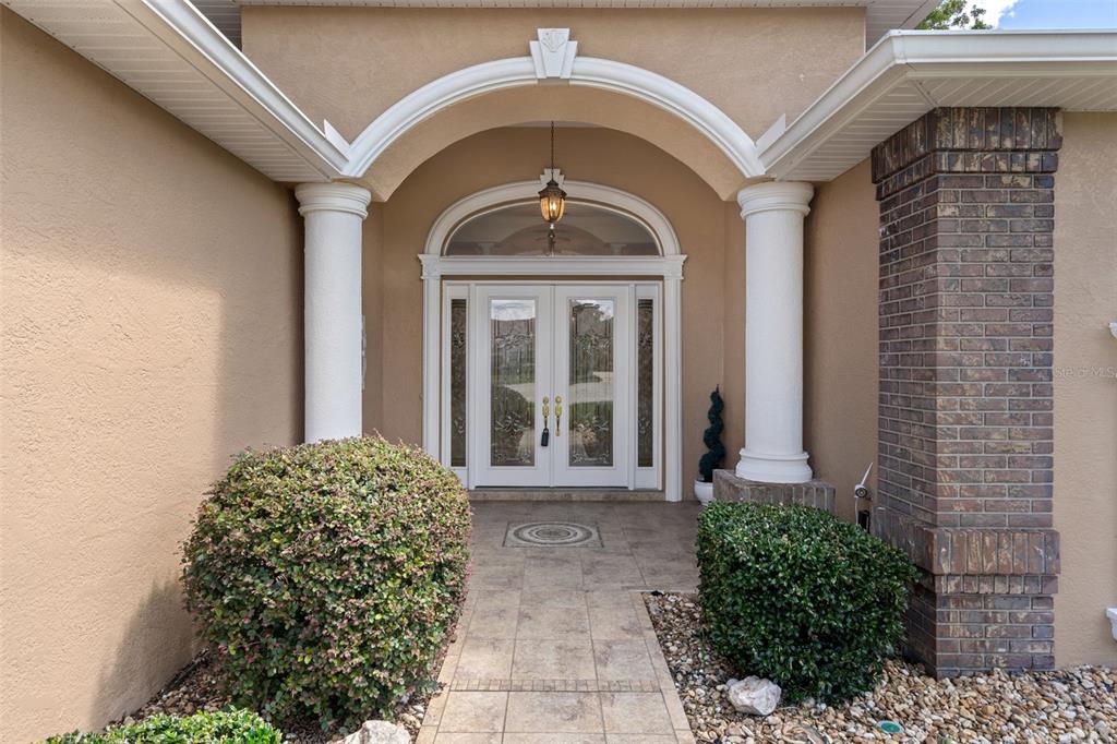 The front entrance features double glass doors under an arched portico with two white columns — 13417 WHITEHAVEN COURT, SPRING HILL, FL