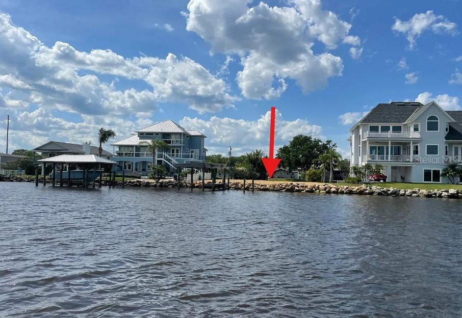 A red arrow points to a vacant waterfront lot situated between two large houses — 989 SHOCKNEY DRIVE, ORMOND BEACH, FL