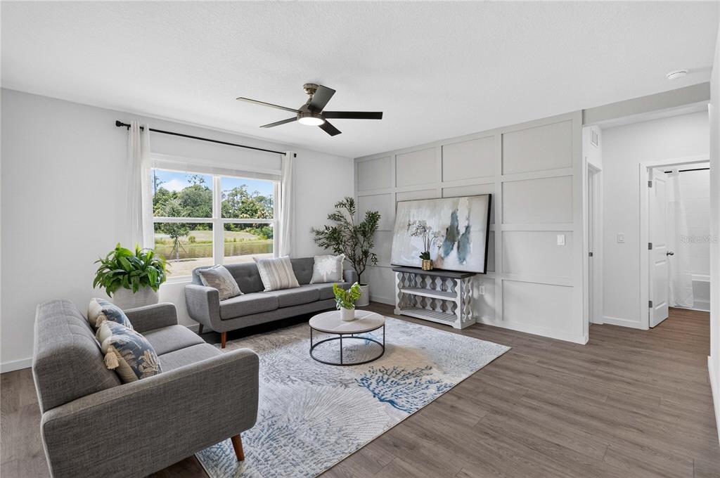 A living room features gray sofas, a patterned rug, and a paneled accent wall — 1037 CHAMPION RIDGE DRIVE, DAYTONA BEACH, FL