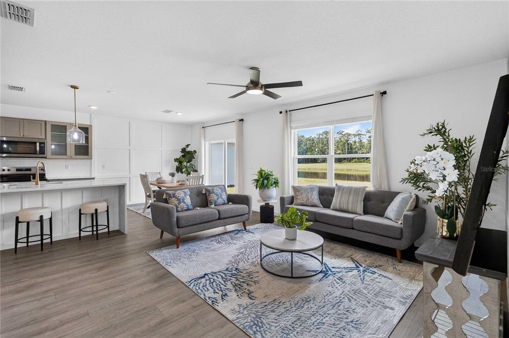 An open-concept living room and kitchen featuring gray sofas, a coastal rug, and large windows — 1037 CHAMPION RIDGE DRIVE, DAYTONA BEACH, FL