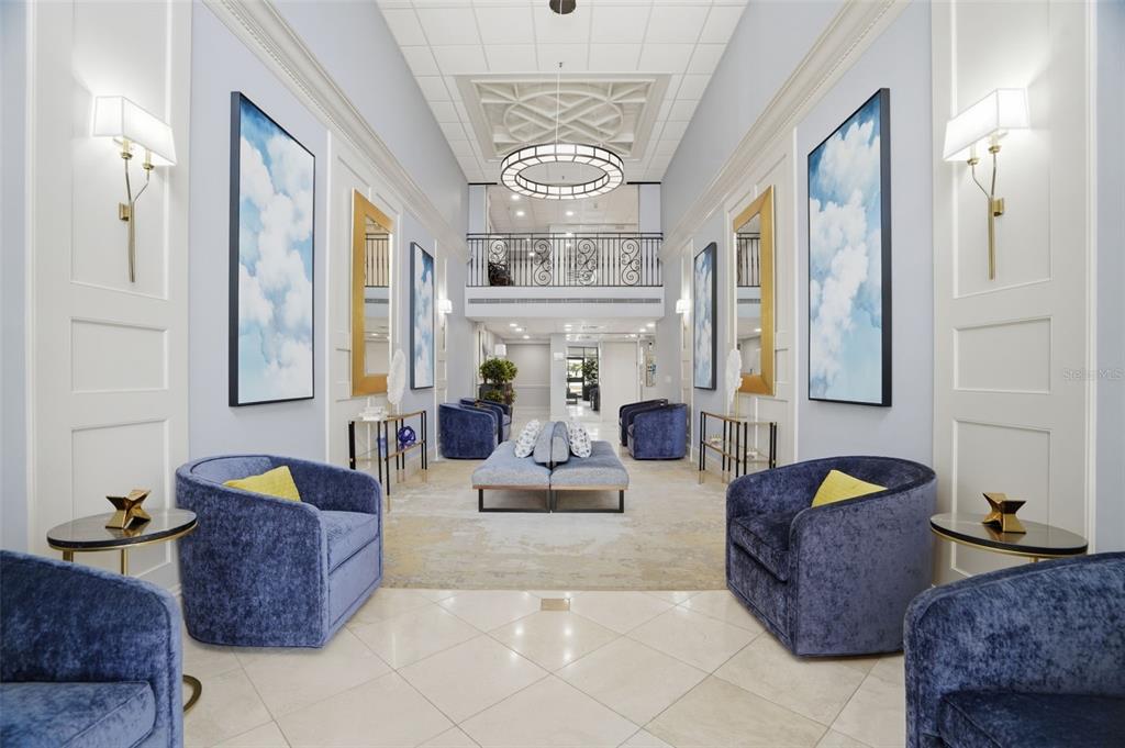 A symmetrical lobby features blue velvet armchairs, cloud artwork, and a central chandelier — 6 BELLEVIEW BOULEVARD UNIT 705, BELLEAIR, FL